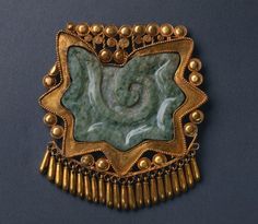 a gold and green brooch with beads around it's edges on a blue background