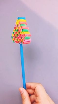 a hand holding a colorful toothbrush with lots of colored straws on top of it