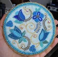 a hand holding a blue and white beaded brooch with birds on it's side