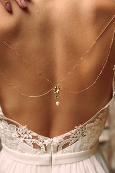 the back of a woman's white dress with a gold cross and pearl necklace