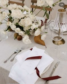 the table is set with white flowers and silverware, napkins, and utensils