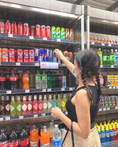 a woman is shopping in a grocery store with many drinks on the shelves behind her