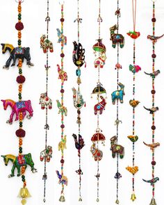 several different types of beaded necklaces hanging on a white wall with bells attached to them