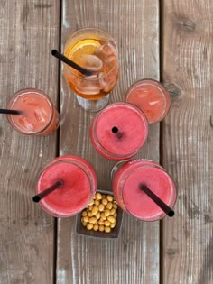 four glasses filled with drinks sitting on top of a wooden table