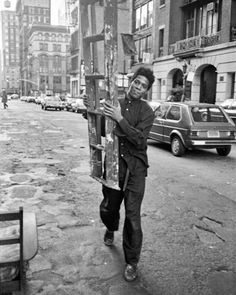 a black and white photo of a man walking down the street carrying a cross on his back