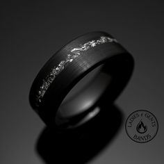 a black wedding band with white gold inlays on the inside of it, against a dark background