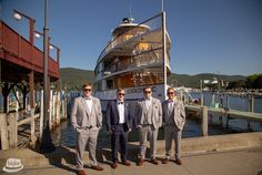 three men in suits standing next to each other near a boat docked at a pier