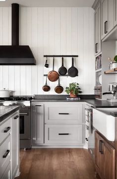 a kitchen with wooden floors and white walls, pots and pans hanging on the wall