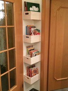 a white shelf with books and magazines on it in front of a wooden door next to a window