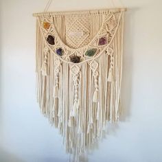 a macrame wall hanging with beads and tassels on a white wall