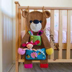 a crocheted teddy bear sitting in a crib with a doll on it