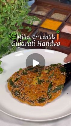 a person is cutting up food on a plate with a knife and some herbs in the background