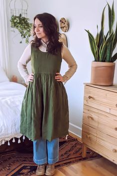 a woman standing in front of a bed wearing a green dress