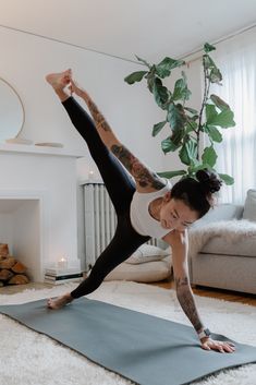 a woman is doing yoga on a mat in front of a fireplace with a potted plant