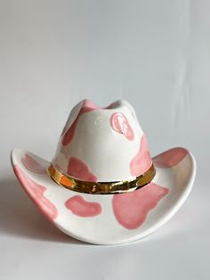 a white hat with pink spots and gold trim on the brim is sitting in front of a white background