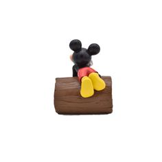 a mickey mouse figurine sitting on top of a piece of wood with yellow feet