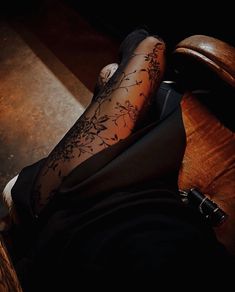 a woman sitting on top of a wooden chair next to a brown leather chair with her legs crossed