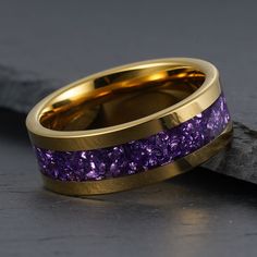 a gold ring with purple stones in it on top of a black stone slab next to a piece of wood