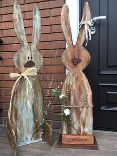 two wooden rabbits sitting next to each other on the ground in front of a door