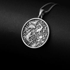 a silver pendant with fish and flowers in the center on a black background, hanging from a chain