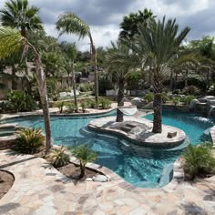 an outdoor swimming pool surrounded by palm trees and rocks with a waterfall in the middle