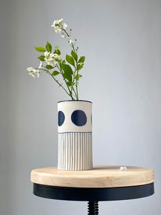 a white and black vase sitting on top of a wooden table with flowers in it