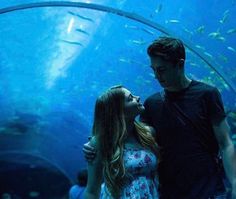 a man and woman standing in front of an aquarium looking at each other with their eyes closed