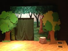 a stage set with trees and curtains on the wall, in front of a wooden floor