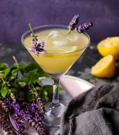 a drink in a glass with lavender sprigs and lemons on the side