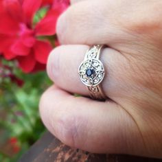 a person's hand with a gold ring on it and red flowers in the background