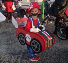 a little boy dressed up as mario in a costume with a car shaped box attached to his chest