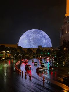 cars are driving down the road in front of a huge blue moon over a city