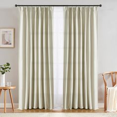 a living room with white walls and curtains on the windowsills, along with a wooden chair