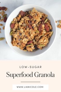 a white bowl filled with granola on top of a table next to nuts and seeds