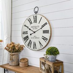 a large clock mounted to the side of a white wall next to a wooden table