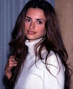 a woman with long brown hair wearing a white turtle neck sweater posing for the camera