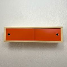 an orange shelf mounted to the side of a white wall with two black dots on it