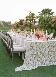 a long table is set up with white chairs and floral centerpieces on it