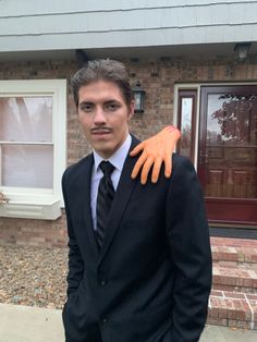 a man in a suit and tie with an orange glove on his shoulder, standing next to a house