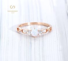 a white opal and diamond ring sitting on top of a wooden table