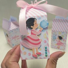 a hand holding up a small gift box with a girl on it's side