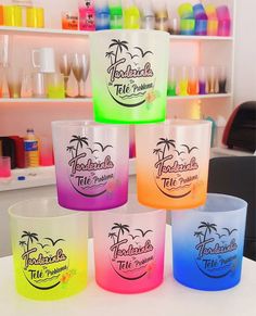 four different colored glasses sitting on top of a white table in front of shelves with bottles