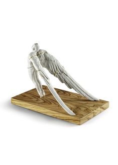 a white angel figurine sitting on top of a wooden board with wings outstretched