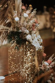 a vase filled with lots of flowers on top of a wooden table covered in lights