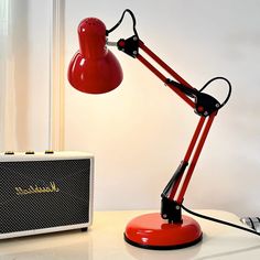 a red desk lamp sitting on top of a table next to a white radio and speaker