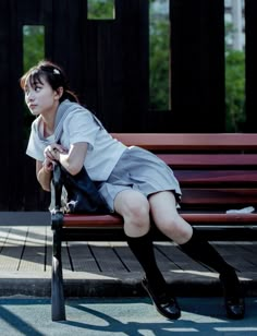 a woman sitting on top of a wooden bench next to a red bench with her legs crossed