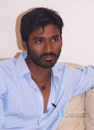 a man sitting on top of a couch next to a white wall and wearing a blue shirt