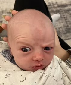 a balding baby is being held up by someone's hand with scissors on their head