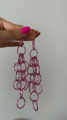 a woman's hand holding up pink earrings with circles hanging from the end of them