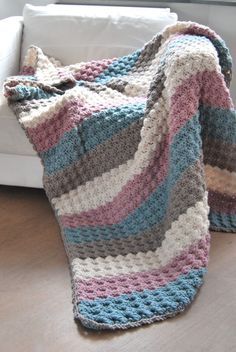 a crocheted blanket sitting on top of a wooden floor next to a white couch